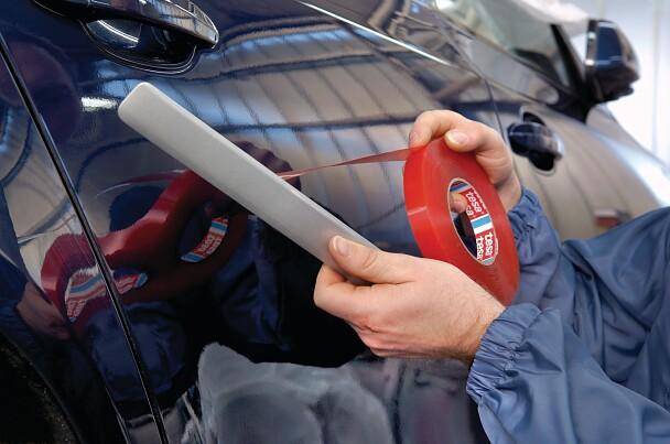 Person wrapping red adhesive tape around a white pole — manual tape application